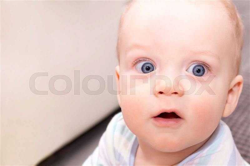 Surprised open-eyed baby boy. Close-up portrait of blue-eyed infant kid. Open-mouthed amazed toddler, stock photo