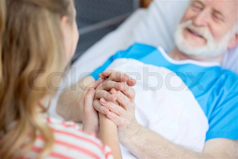 Patient grandfather and child holding hands in hospital bed, stock photo