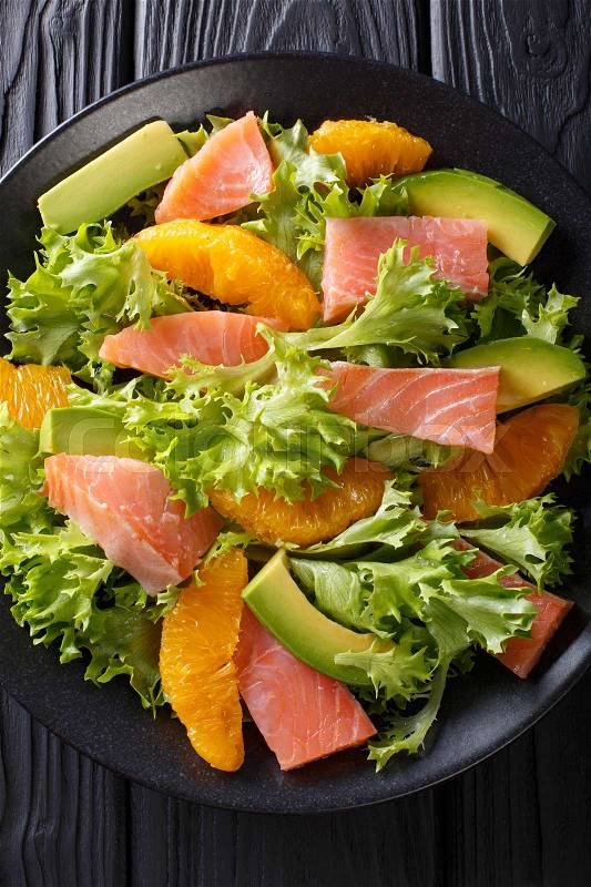 Beautiful food: salad of salted salmon, oranges, avocado and lettuce close-up on a plate on a table. Vertical view from above , stock photo