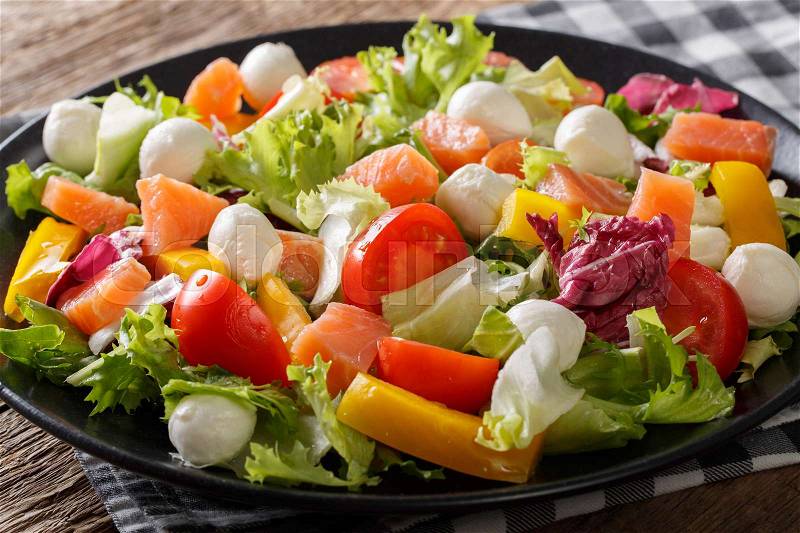 Fresh salad with salted salmon, mozzarella cheese and vegetables close-up on a plate. horizontal , stock photo