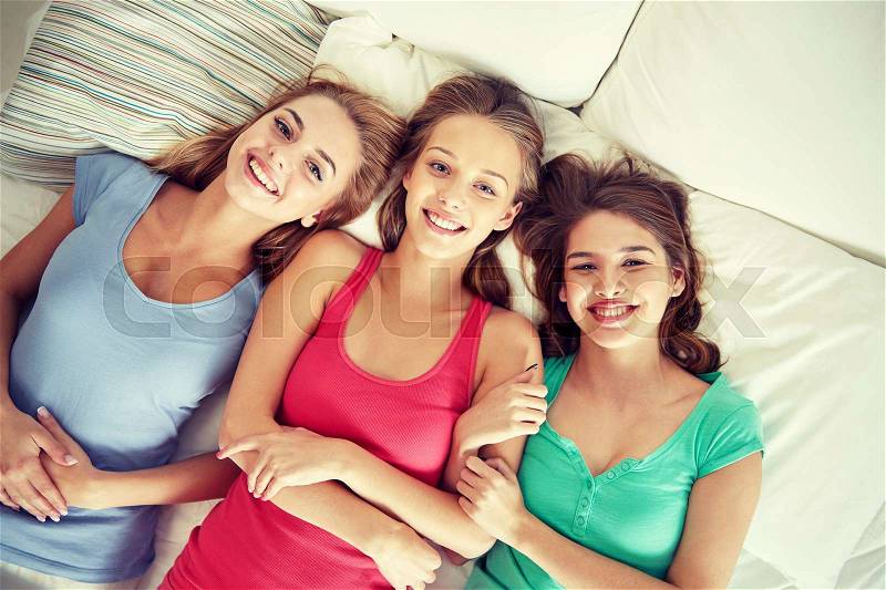Friendship, people and pajama party concept - happy friends or teenage girls having fun and lying in bed at home, stock photo