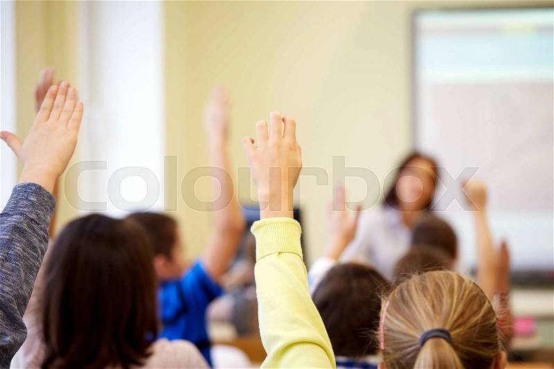Education, elementary school, learning and people concept - group of students raising hands on lesson in classroom, stock photo