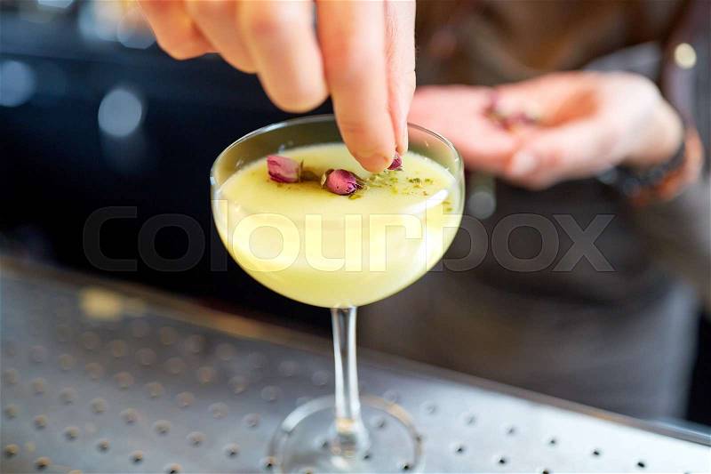 Alcohol drinks, people and luxury concept - bartender hand decorating cocktail in glass with dried flowers at bar, stock photo