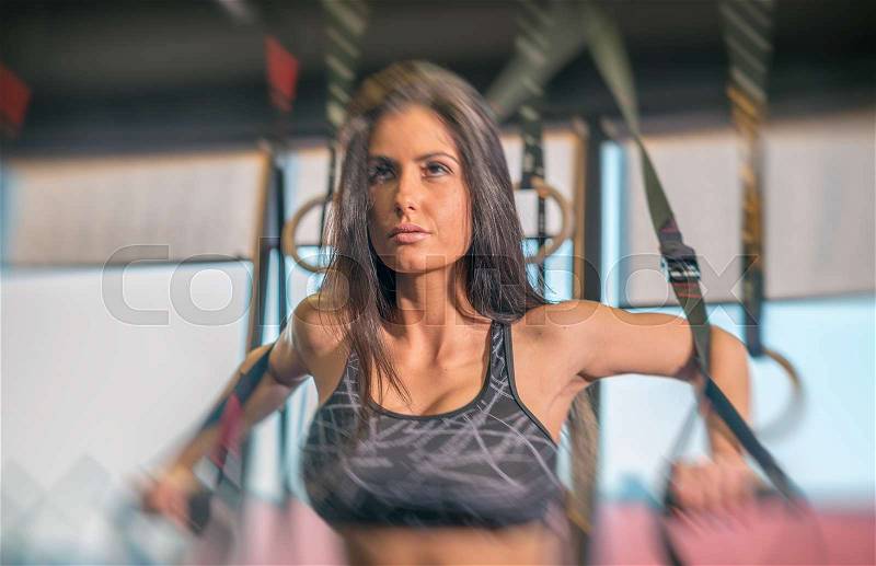 Beautiful brunette girl exercising with rings at gym, stock photo
