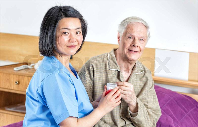 Nurse sgiving pill to elderly man in hospital bed, stock photo