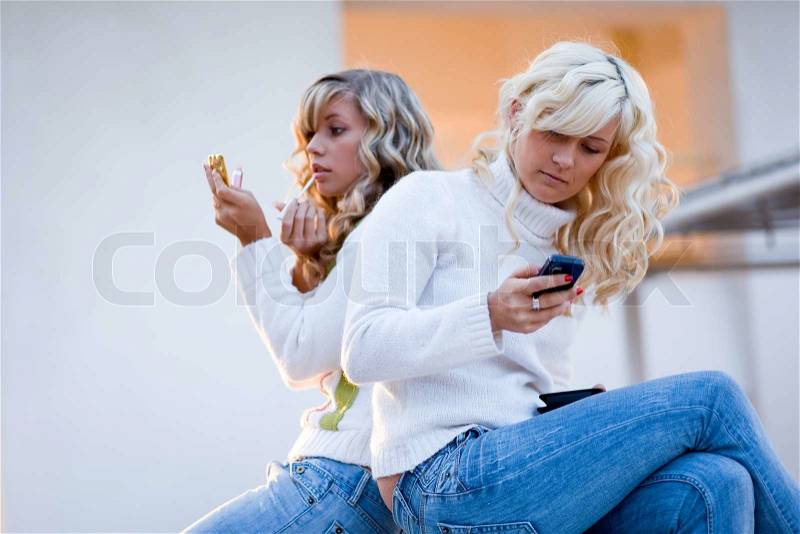 Two teenage girls sit and talking watching mobile phone, stock photo