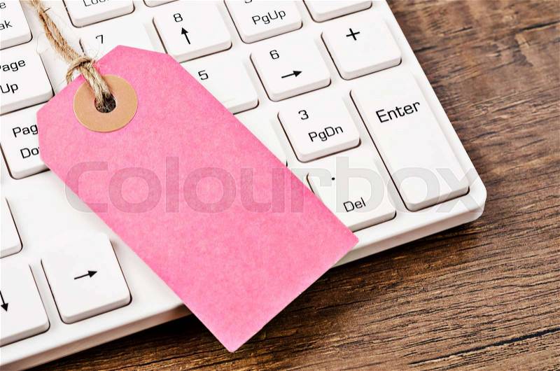 Blank pink label or tag price with white computer keyboard on wooden background, stock photo