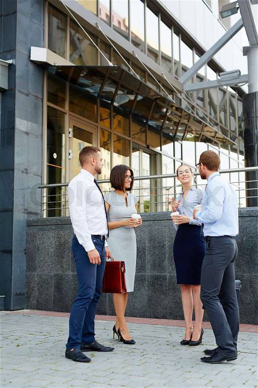 Group of young successful business people chatting outside office building during break, stock photo