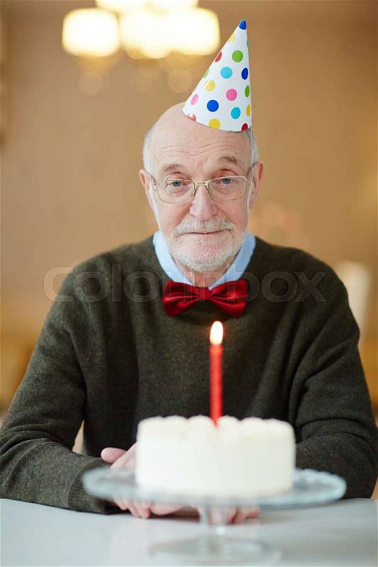Sad senior man sitting by table with birthday cake, stock photo