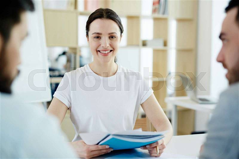 Portrait of smiling young woman working in office meeting with clients and looking at camera, stock photo