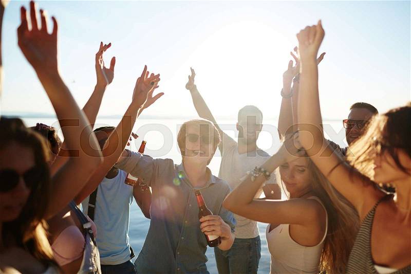 Ecstatic buddies dancing with raised hands at beach party, stock photo