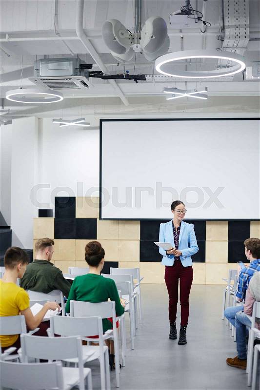 Young teacher making speech in front of audience in lecture hall, stock photo