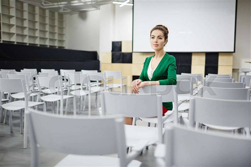 Young teacher or student sitting in row on one of chairs in lecture hall, stock photo