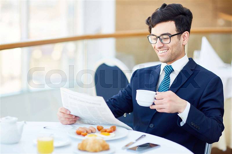 Smiling businessman drinking tea or coffee and reading newspaper in cafe, stock photo