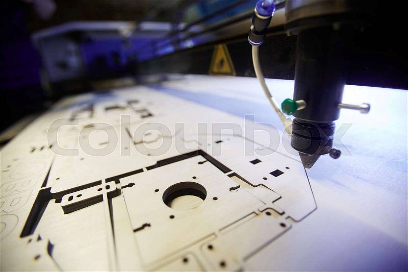 Laser engraving machine cutting details from plywood sheet, stock photo