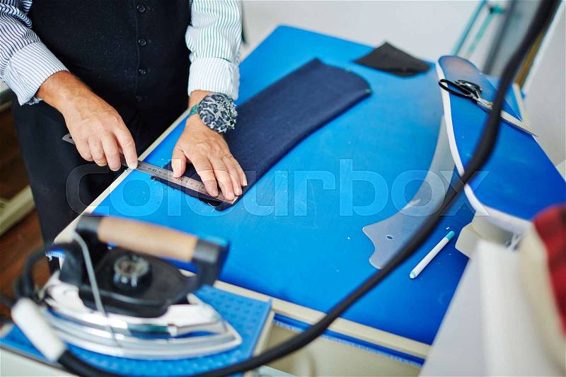 Closeup portrait of elegant old man making clothes in old fashioned tailoring studio, cutting cloth to patterns on working table, stock photo