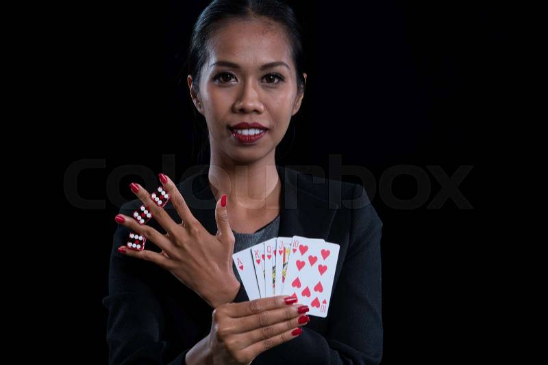 Portrait the female banker clamp red dices between her fingers and holding hearts suit straight flush at casino, with chips and banknotes on a green blackjack table, stock photo