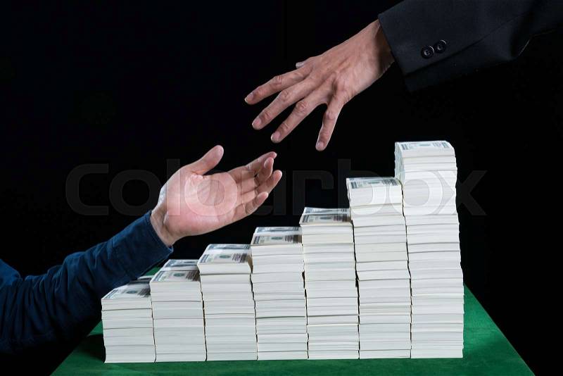 Hand of the Businessman is reaching out to help other hand against the stack of dollars placed on green table, black background in the growth business financial concept , stock photo