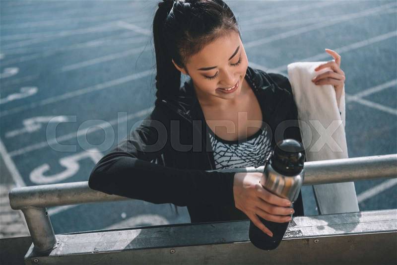 Asian sportswoman with sport bottle and towel on running track on stadium, stock photo