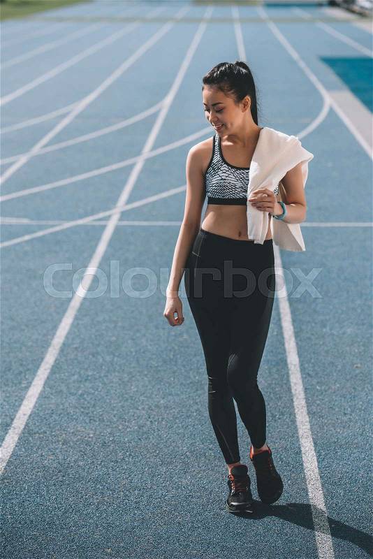 Smiling young sportswoman with towel standing on running track stadium , stock photo