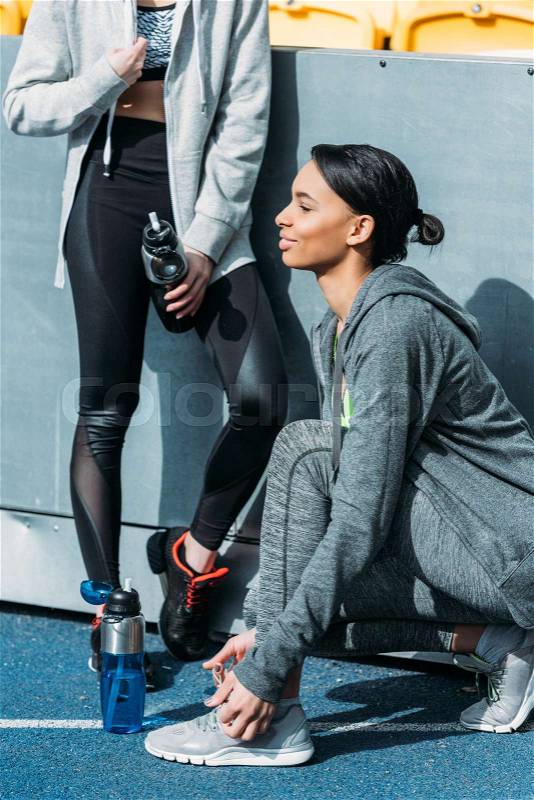 Athletic young women in sportswear resting with sports bottles on stadium, running women concept, stock photo