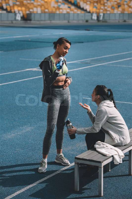 Athletic young women in sportswear drinking water from sports bottles on stadium, running women concept, stock photo