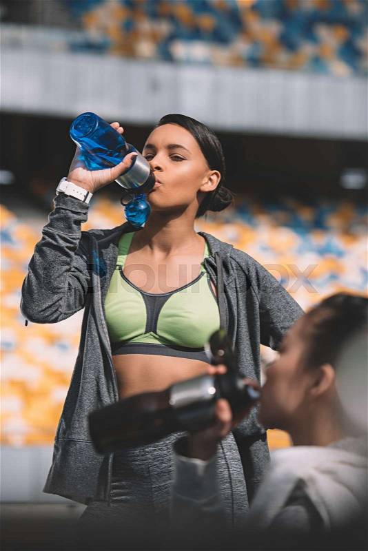 Attractive young sportswoman drinking water from bottle and looking at friend, running woman tired concept , stock photo