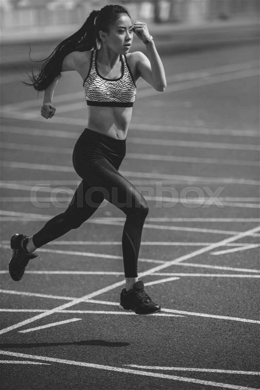 Athletic young sportswoman sprinting on running track stadium, black and white photo, stock photo