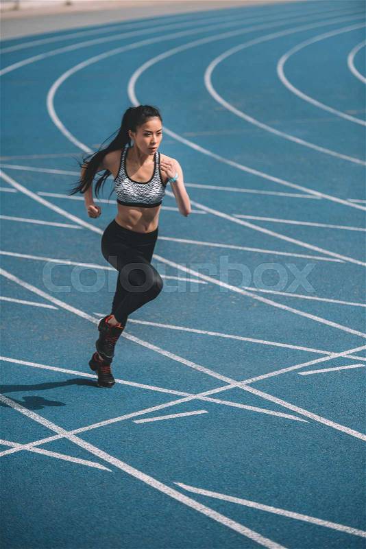 Athletic young sportswoman sprinting on running track stadium, stock photo