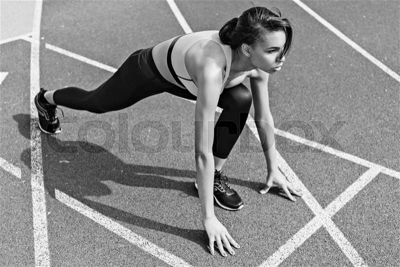 Concentrated athletic young runner on starting line at running track stadium, black and white photo, stock photo