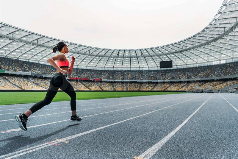 Athletic young woman in sportswear sprinting on running track stadium, stock photo