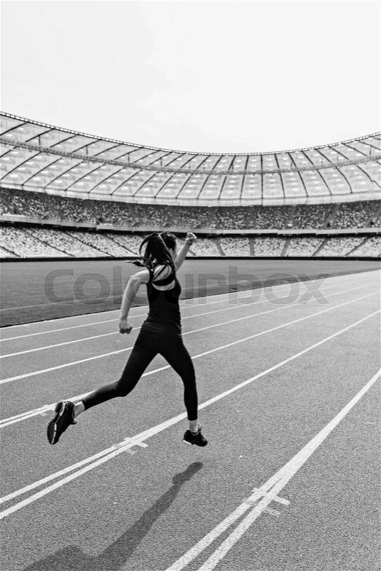 Back view of young fitness woman in sportswear sprinting on running track stadium, black and white photo , stock photo