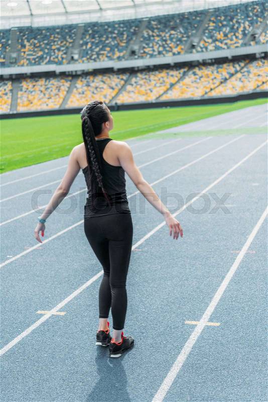 Back view of young fitness woman in sportswear standing on running track stadium, stock photo