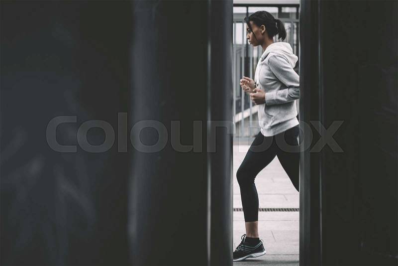 Side view of young fitness woman in sportswear jogging on stadium , stock photo