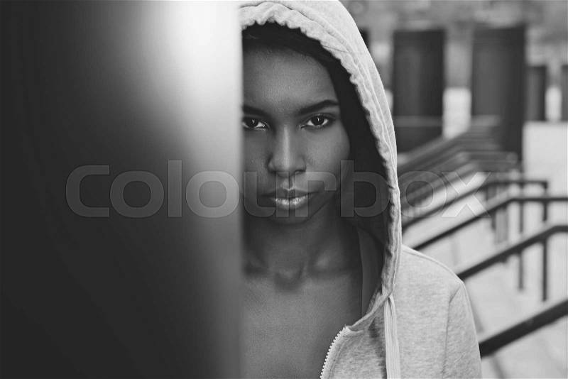 Black and white photo of beautiful young sportswoman in hood looking at camera, stock photo