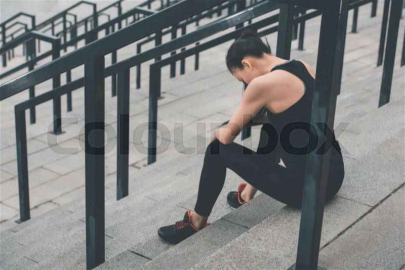 Young tired sportswoman in sportswear sitting on stadium stairs, stock photo