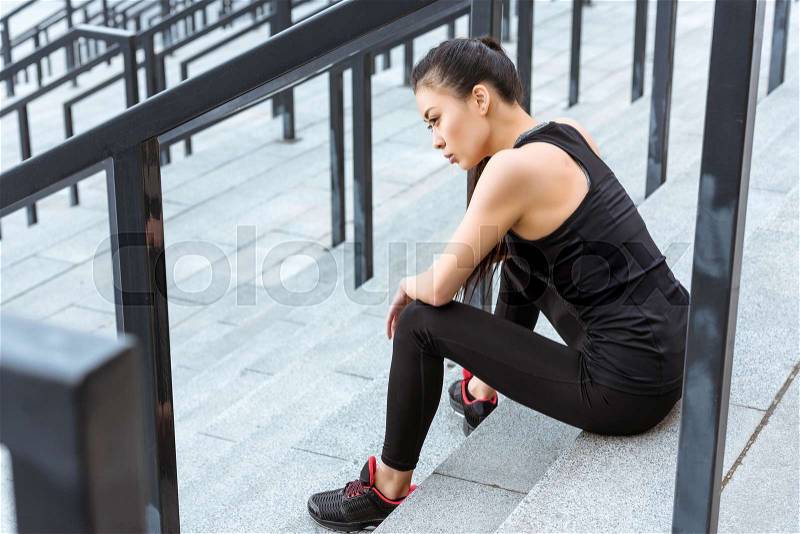 Young tired sportswoman in sportswear sitting on stadium stairs, stock photo