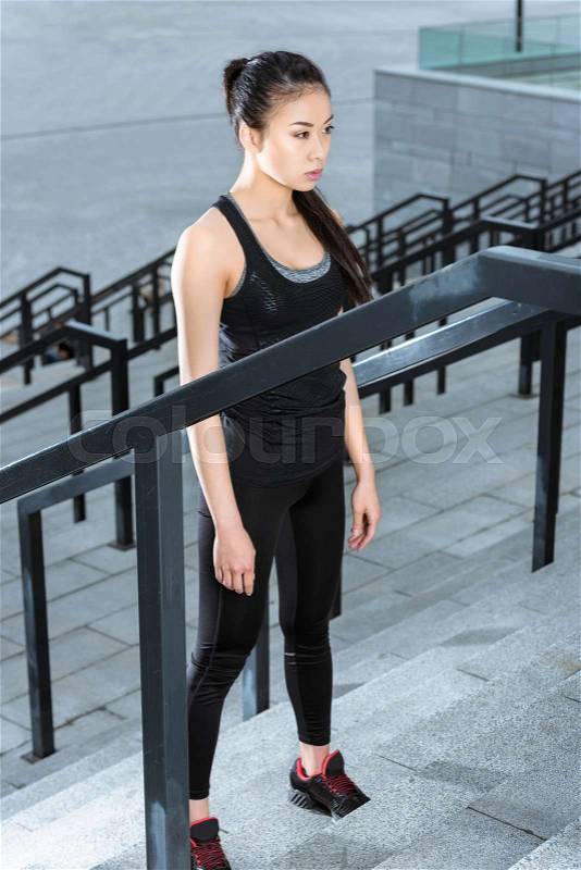 Attractive young woman in sportswear training on stadium stairs and looking away, stock photo