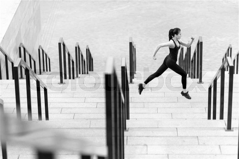 Side view of athletic young woman in sportswear running on stadium stairs, black and white photo, stock photo