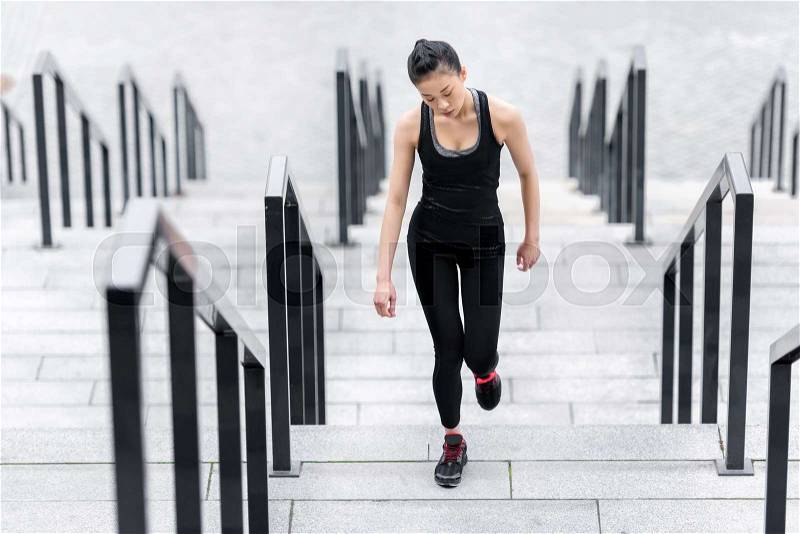Athletic young woman in sportswear running up on stadium stairs, stock photo