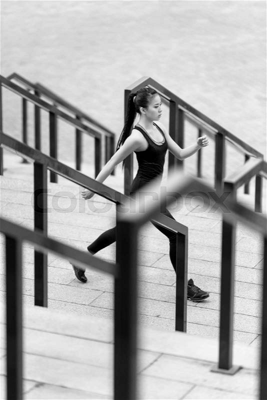 Young sporty asian woman in sportswear jogging on stadium stairs, black and white photo, stock photo