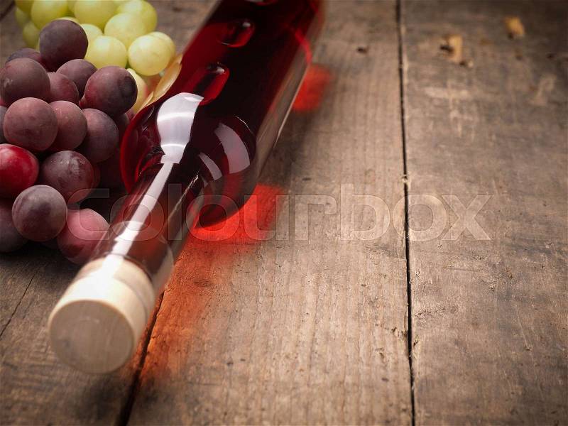 Bottle of red wine with grapes on a rustic wooden table with space for text, stock photo
