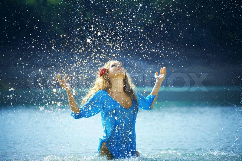 Portrait of young beautiful woman in lake making water splashes, stock photo