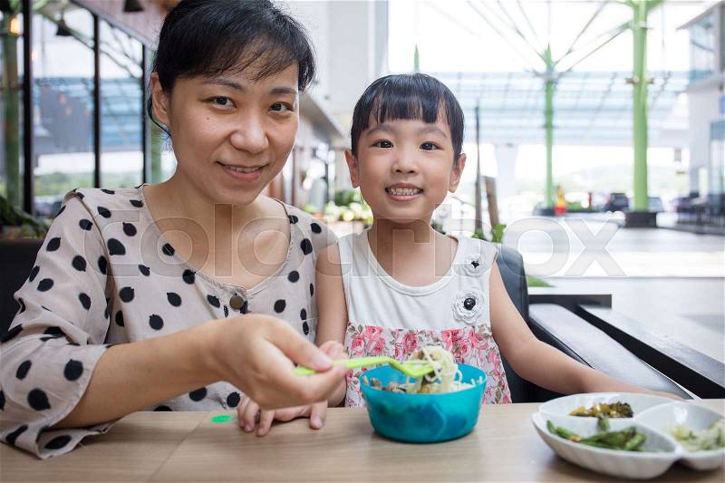 Asian Chinese mother and daughter eating beef noodles in outdoor cafe, stock photo