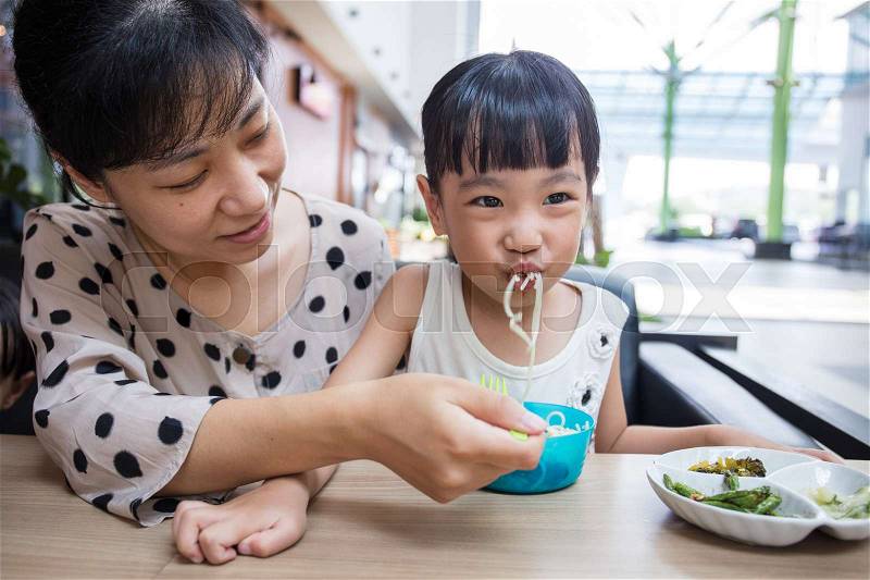Asian Chinese mother and daughter eating beef noodles in outdoor cafe, stock photo