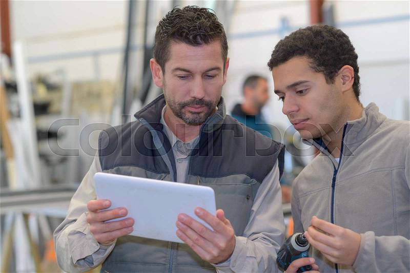 Supervisor and manual worker using digital tablet in metal industry, stock photo
