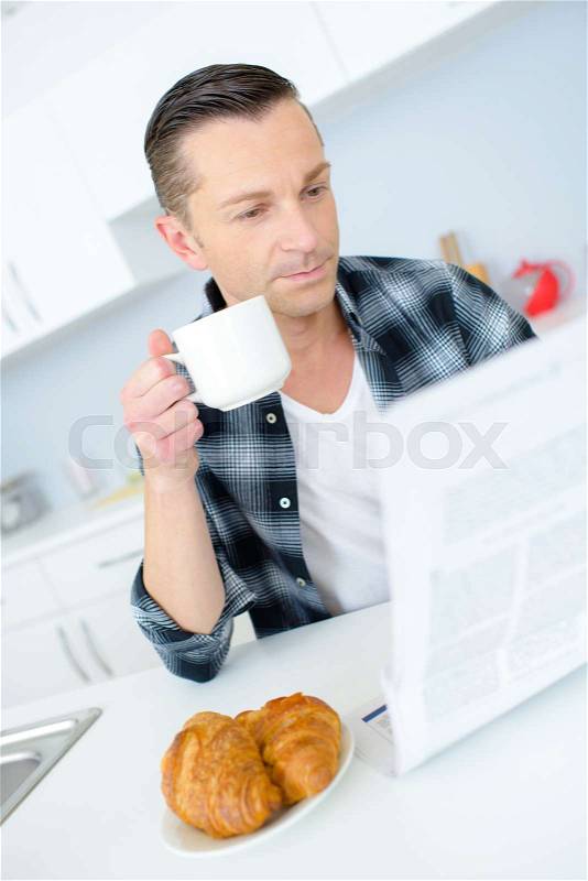Happy young man having breakfast and reading the newspapers, stock photo