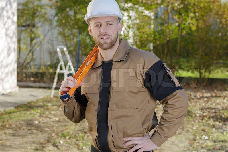 Smiling home inspector holding a level at construction site, stock photo