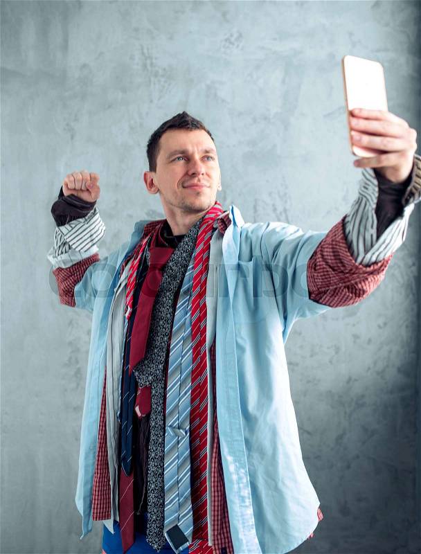 Male buyer dressed in many clothes makes selfie on phone camera at the clothing store. Shopping concept, stock photo