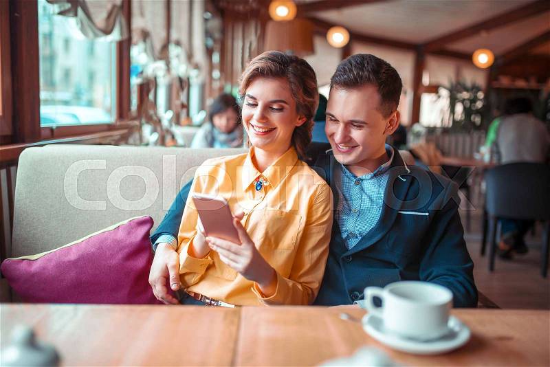 Love couple looks on phone photo album, restaurant on background. Man and woman happy together, stock photo